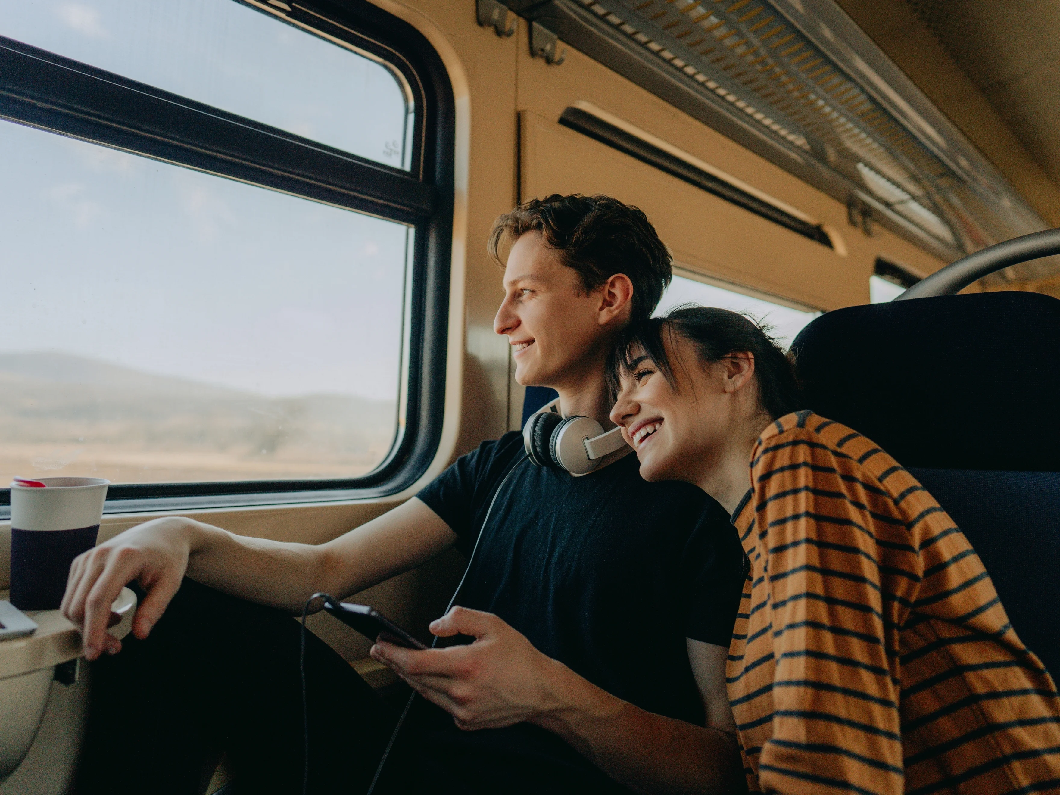 Chico y chica jóvenes sonriendo y sentados en el interior de un tren