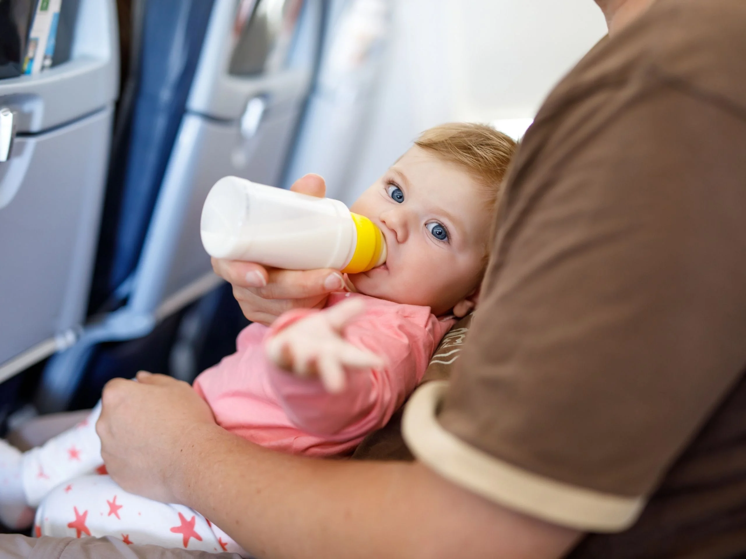 Bebé en avión bebiendo biberón en los brazos de su padre