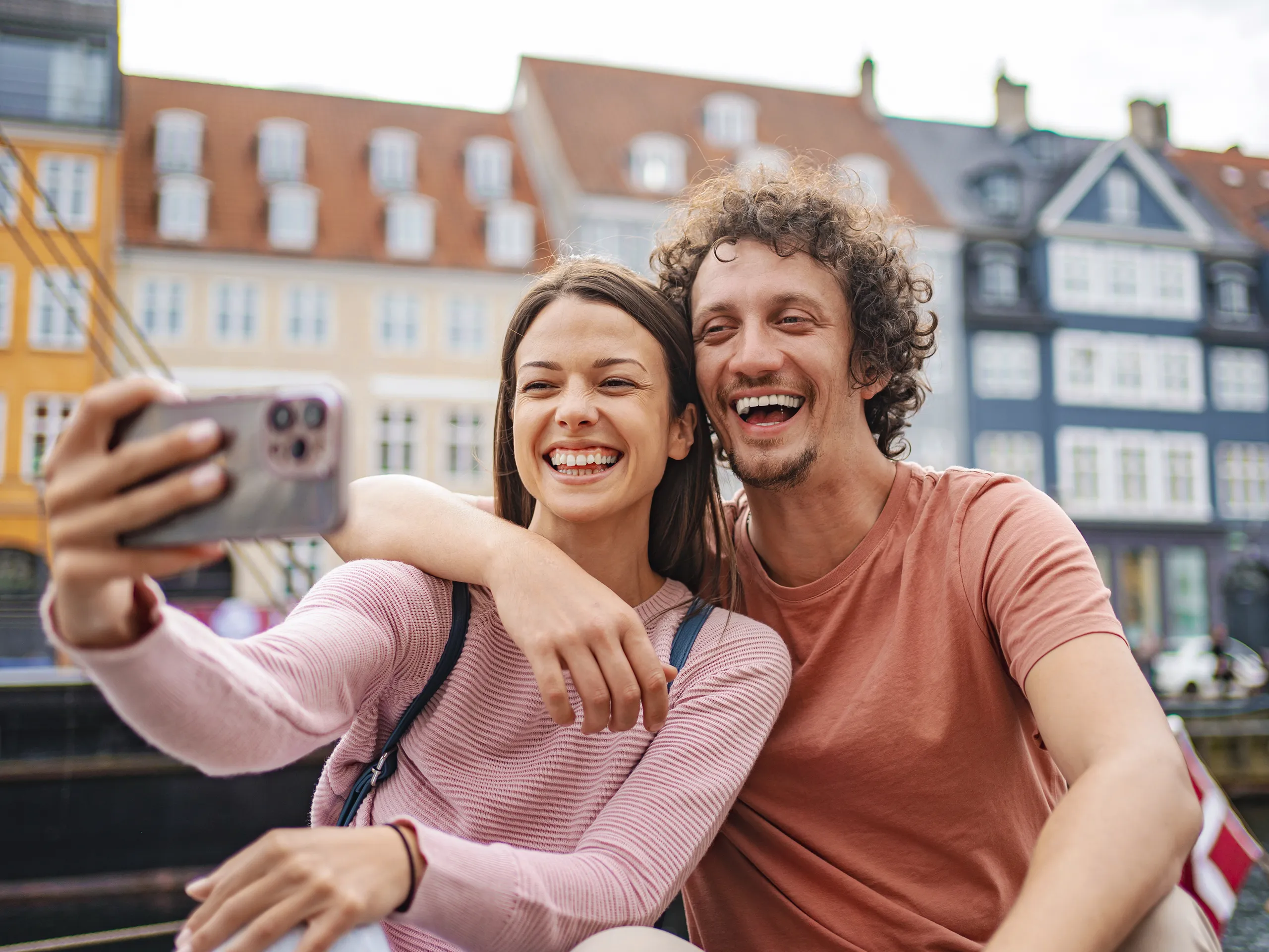 Pareja sonriente tomándose un selfie frente a edificios históricos.