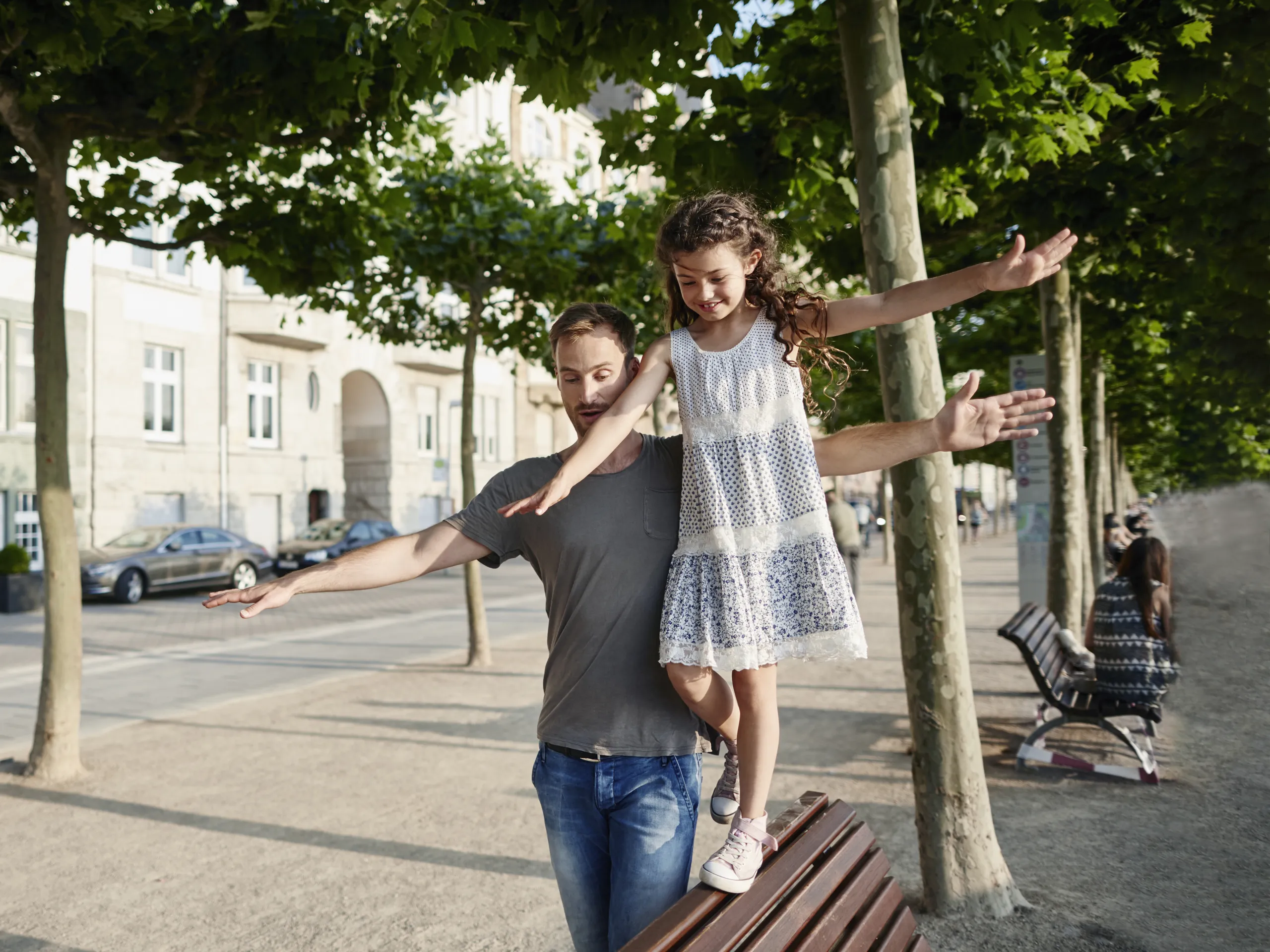 El padre equilibra a su hija en un banco del parque en verano.