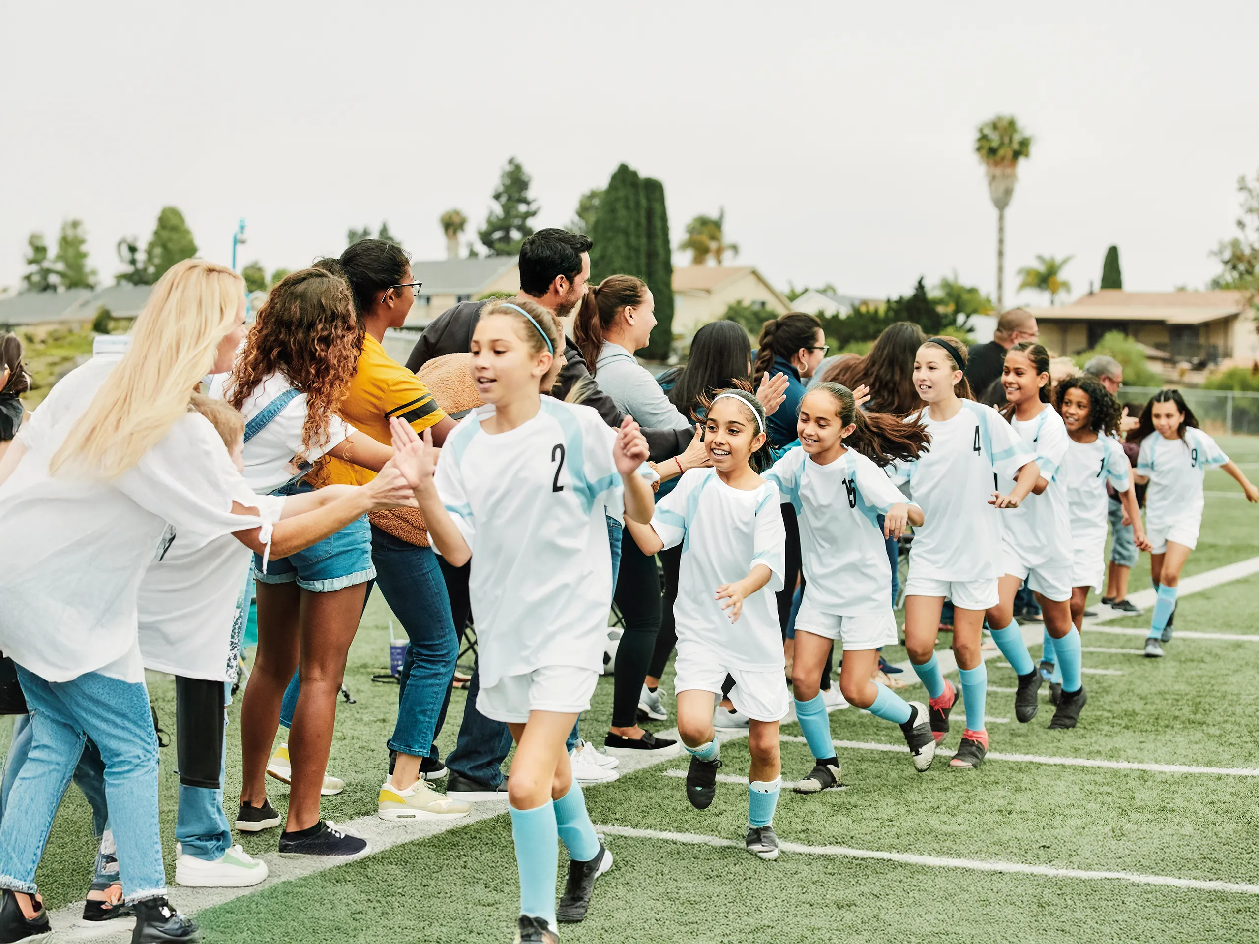 El equipo de fútbol femenino corre pasando junto a los espectadores que los vitorean.