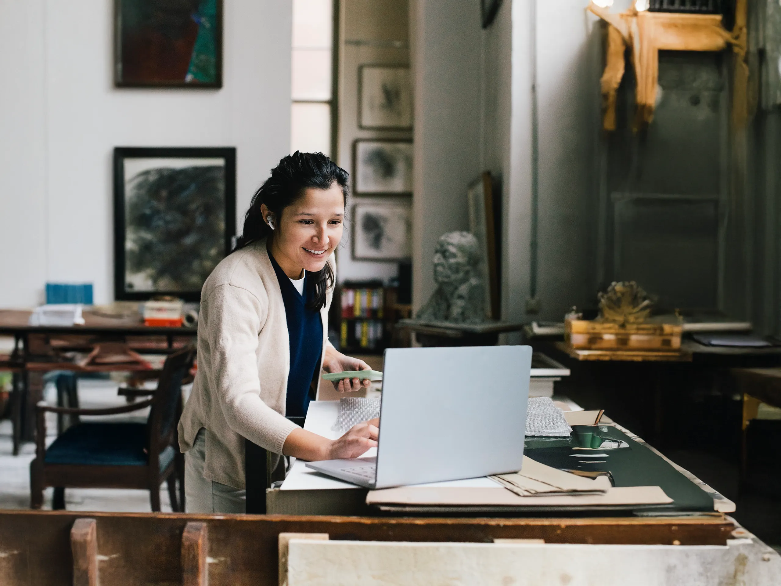 Mujer sonriente trabajando en una computadora portátil en un concurrido estudio de arte.