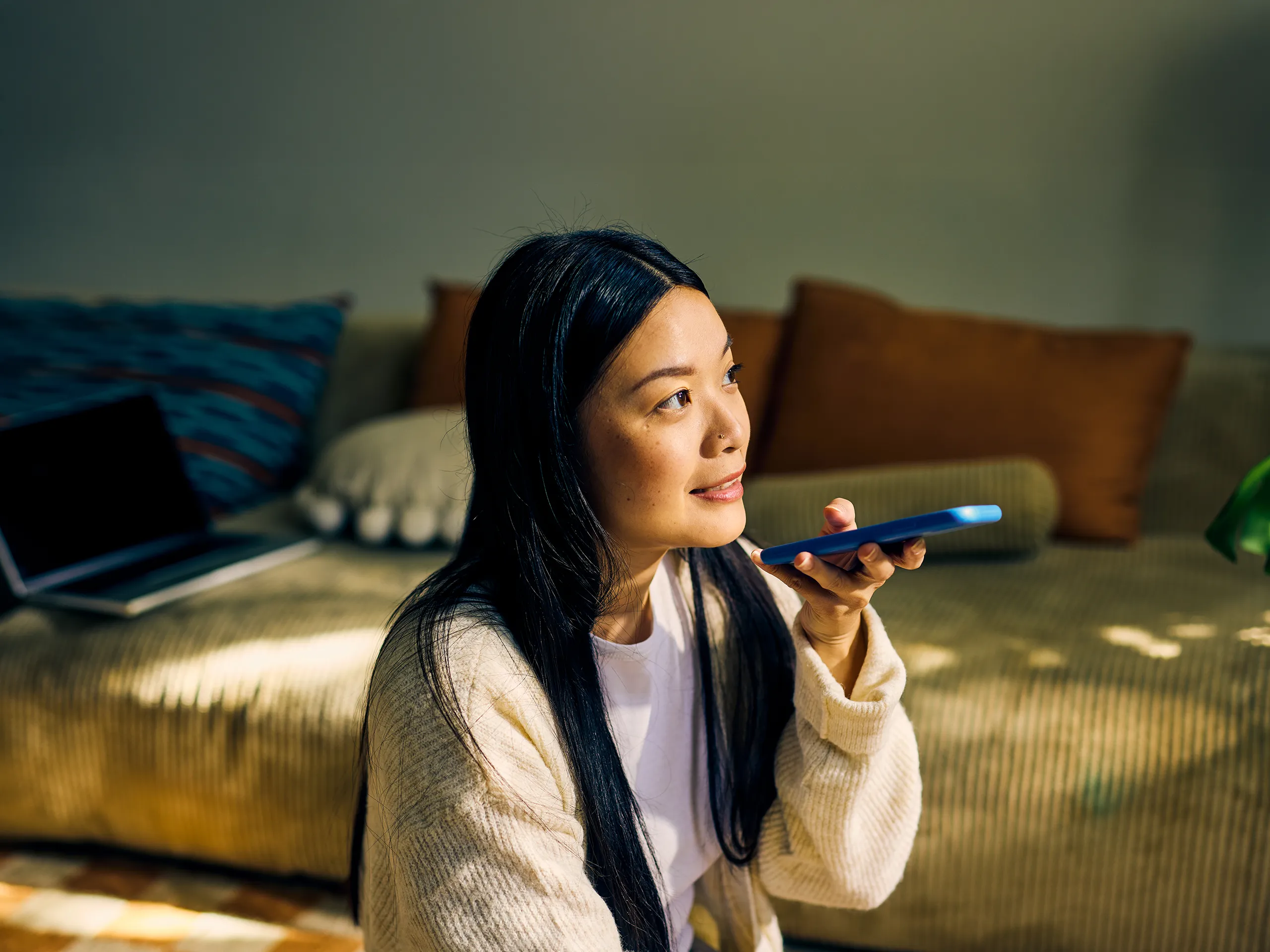 Mujer sentada en el suelo grabando un mensaje de voz en su teléfono inteligente.