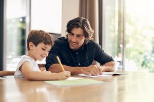 Padre blanco ayudando a su hijo con los deberes en una mesa 