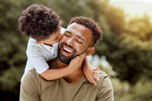 Niño negro besando a su padre en la mejilla en el exterior, felices