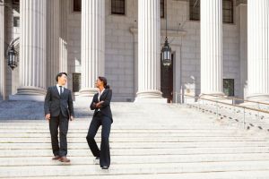 Hombre asiático y mujer negra vestidos de traje chaqueta en las escaleras de un juzgado