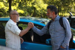 Dos hombres blancos dándose la mano, de fondo un coche. 