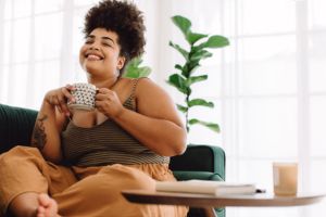 Mujer de talla grande sentada en el sofá, sonriendo y tomando un café