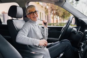 Mujer madura poniéndose el cinturón en el asiento del conductor de un coche y sonriendo a cámara