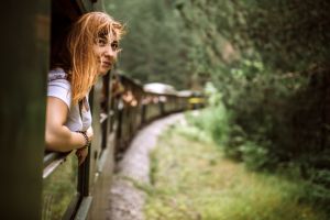 Mujer blanca asomada a la ventana de un tren en movimiento que pasa por un bosque