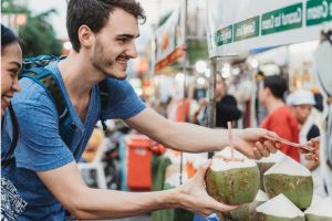Pareja de hombre blanco y mujer asiática de viaje, comprando bebida de coco en un mercado callejero
