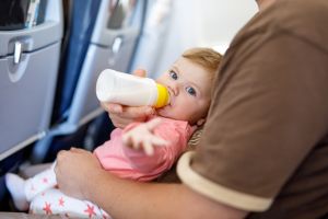 Bebé rubio con ojos azules tomando el biberón en un avión
